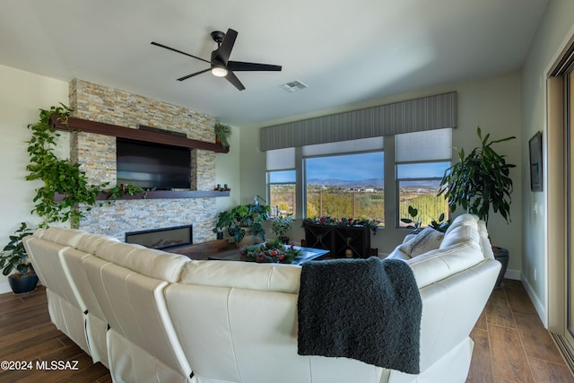 living room featuring dark hardwood / wood-style floors, ceiling fan, and a stone fireplace