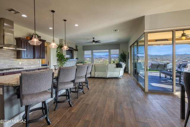 kitchen with dark hardwood / wood-style flooring, tasteful backsplash, ceiling fan, wall chimney range hood, and hanging light fixtures