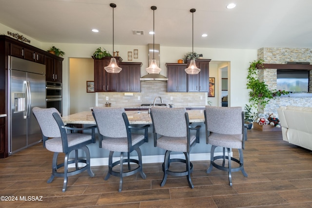 kitchen featuring pendant lighting, wall chimney exhaust hood, stainless steel appliances, and dark hardwood / wood-style floors