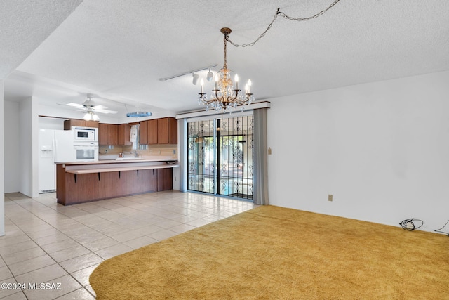 kitchen featuring decorative light fixtures, light tile patterned floors, white appliances, kitchen peninsula, and a textured ceiling