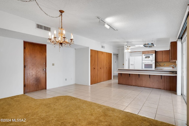 kitchen with light tile patterned flooring, a textured ceiling, kitchen peninsula, white appliances, and ceiling fan with notable chandelier