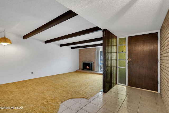 unfurnished living room with light colored carpet, beam ceiling, a large fireplace, and a textured ceiling