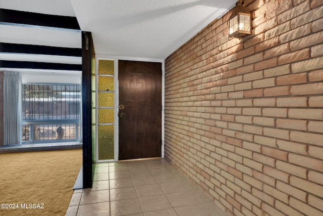 entrance foyer featuring light tile patterned floors, a textured ceiling, and brick wall