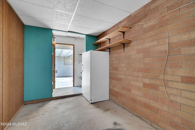 interior space featuring white refrigerator, a paneled ceiling, brick wall, and wood walls