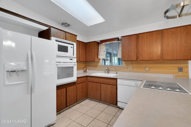 kitchen featuring sink, white appliances, a skylight, and light tile patterned floors