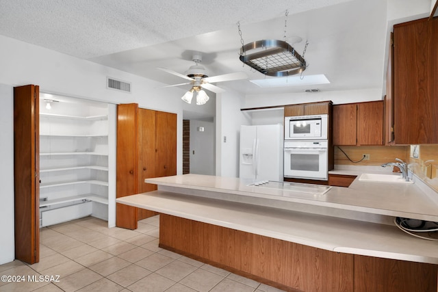 kitchen with sink, a textured ceiling, light tile patterned floors, kitchen peninsula, and white appliances