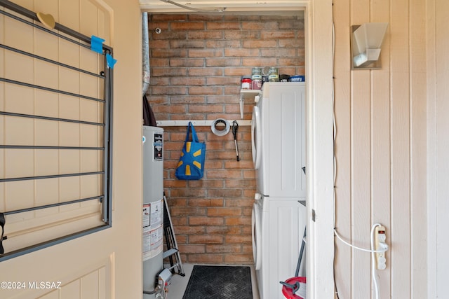 interior space featuring gas water heater, stacked washer / drying machine, and brick wall