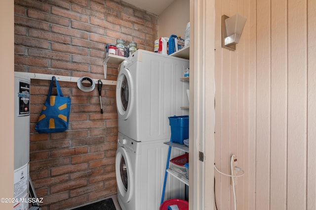 washroom with stacked washer / dryer and brick wall