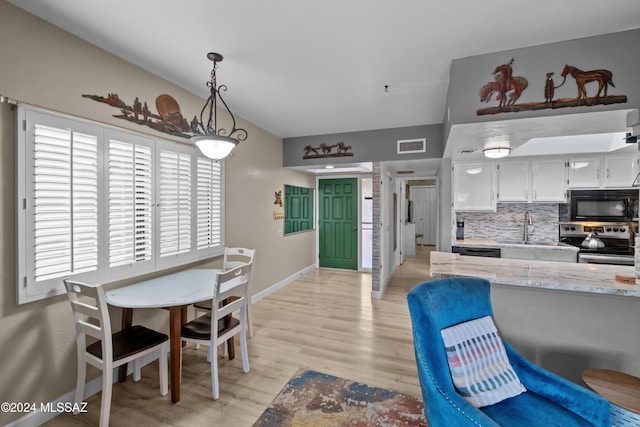 kitchen with black appliances, white cabinets, sink, hanging light fixtures, and light hardwood / wood-style floors