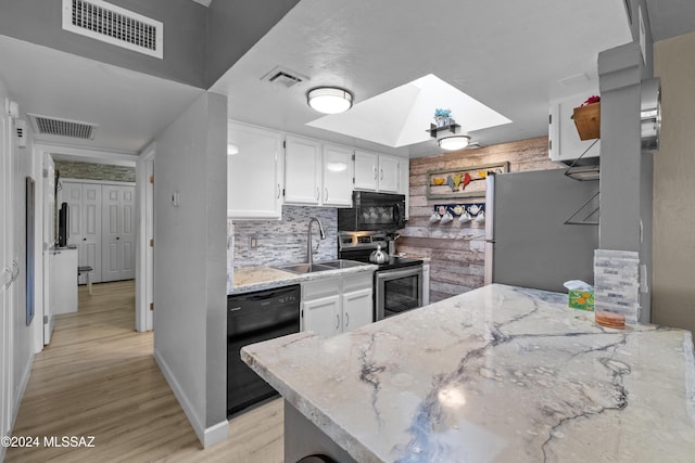 kitchen with a skylight, white cabinetry, sink, black appliances, and light wood-type flooring