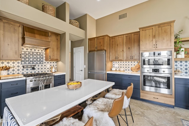 kitchen featuring light stone countertops, stainless steel appliances, premium range hood, gray cabinets, and decorative backsplash