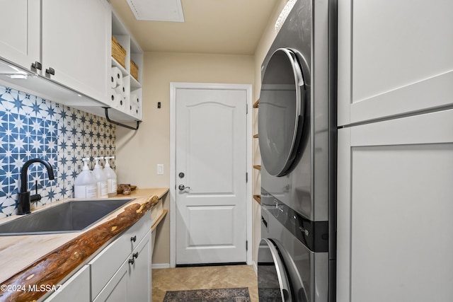 clothes washing area featuring cabinets, stacked washing maching and dryer, and sink