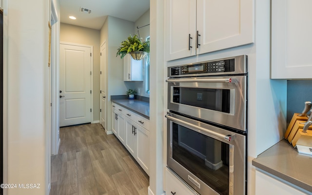 kitchen with white cabinets, light wood-type flooring, and stainless steel double oven