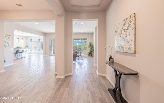 hallway with light wood finished floors, visible vents, and baseboards