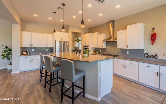 kitchen featuring white cabinets, wall chimney exhaust hood, pendant lighting, and appliances with stainless steel finishes