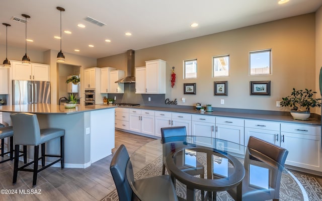 kitchen featuring white cabinets, wall chimney exhaust hood, pendant lighting, and appliances with stainless steel finishes