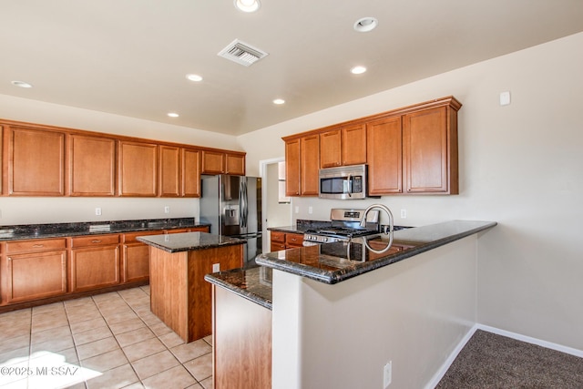 kitchen with light tile patterned floors, stainless steel appliances, dark stone countertops, and a kitchen island