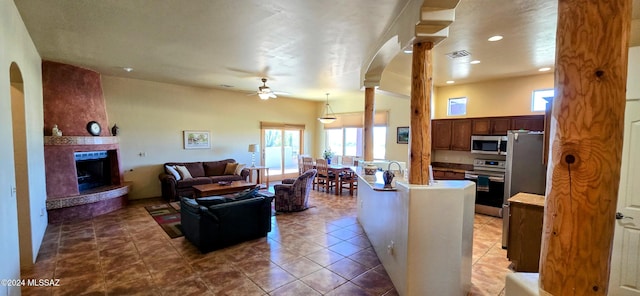 living room featuring plenty of natural light, ceiling fan, a fireplace, and decorative columns