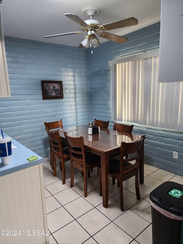 dining area featuring ceiling fan, light tile patterned flooring, and brick wall