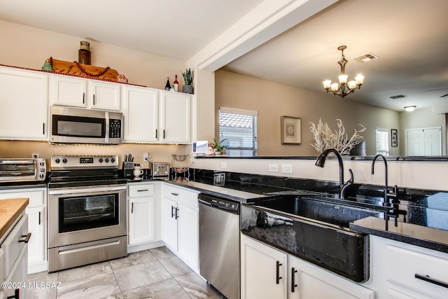 kitchen featuring white cabinetry, sink, an inviting chandelier, and appliances with stainless steel finishes