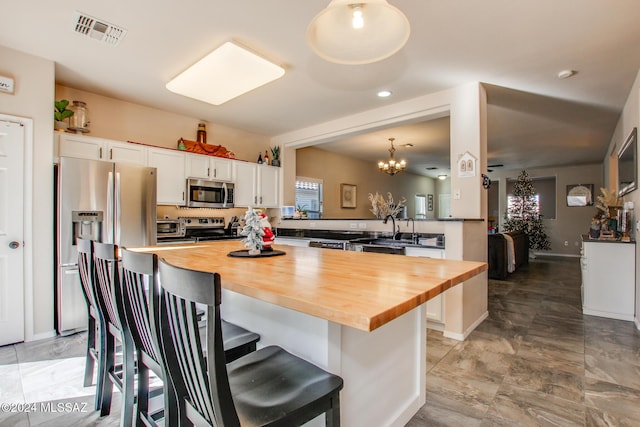 kitchen with butcher block counters, white cabinetry, stainless steel appliances, kitchen peninsula, and a kitchen bar