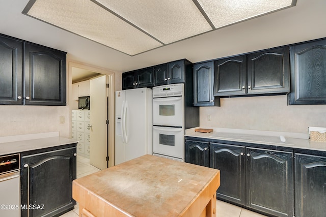 kitchen featuring dark cabinets, white appliances, light countertops, and light tile patterned flooring