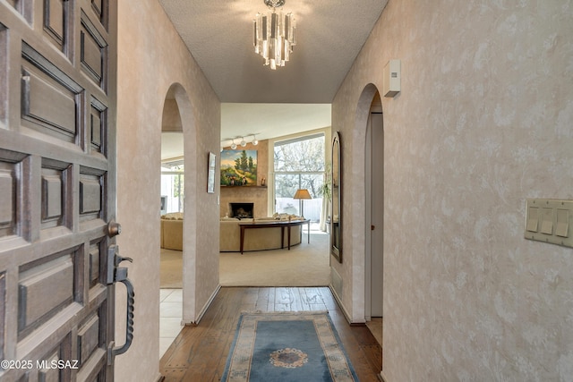 foyer entrance with arched walkways, lofted ceiling, hardwood / wood-style flooring, a fireplace, and a chandelier