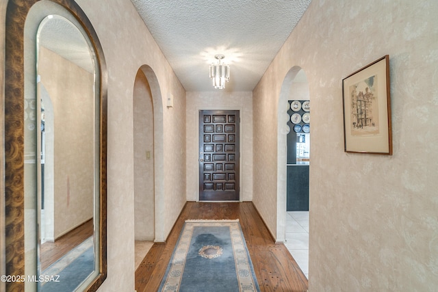 entryway featuring arched walkways, a textured wall, a textured ceiling, a notable chandelier, and hardwood / wood-style floors