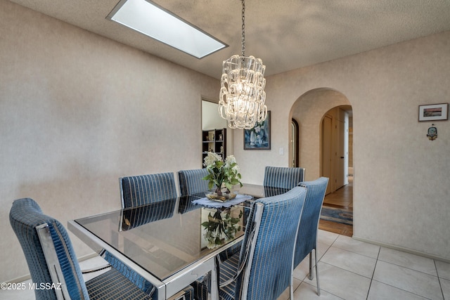 dining space featuring arched walkways, a notable chandelier, and light tile patterned floors