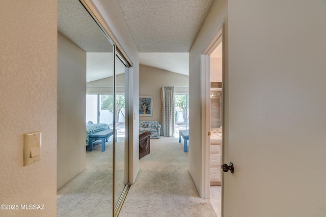 corridor with a textured ceiling, light carpet, and lofted ceiling