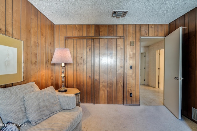 sitting room featuring light carpet, wood walls, visible vents, and a textured ceiling