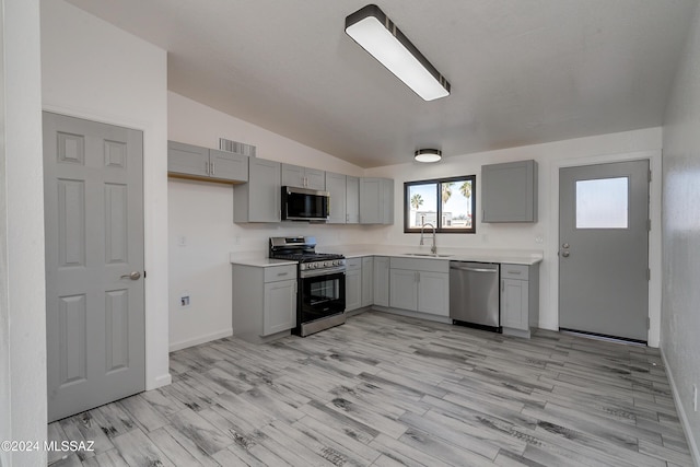 kitchen with gray cabinetry, sink, lofted ceiling, and stainless steel appliances