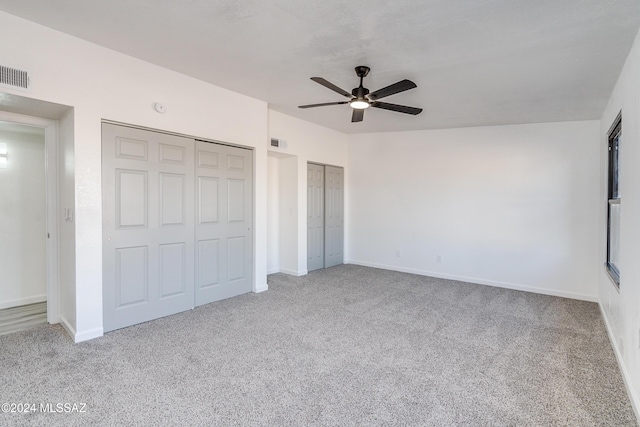 unfurnished bedroom with ceiling fan, light colored carpet, and two closets