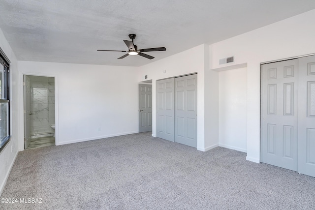 unfurnished bedroom with carpet flooring, a textured ceiling, two closets, ceiling fan, and connected bathroom