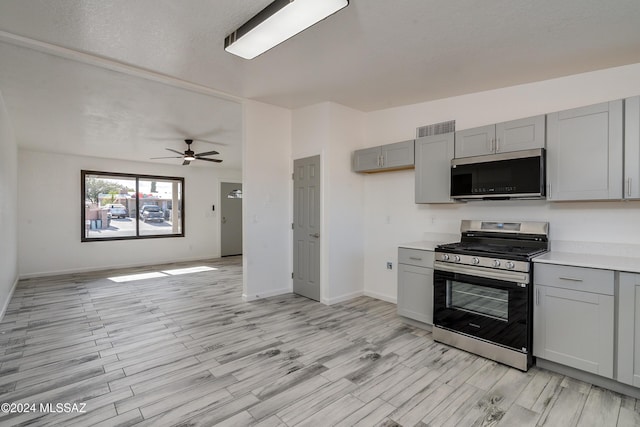 kitchen with appliances with stainless steel finishes, light wood-type flooring, gray cabinetry, a textured ceiling, and ceiling fan