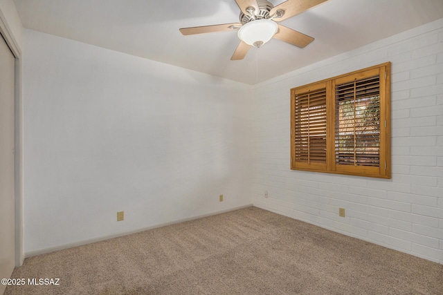 carpeted spare room featuring ceiling fan and brick wall