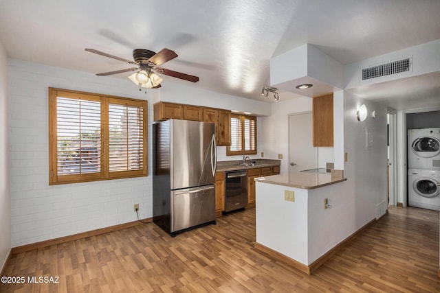 kitchen featuring stainless steel refrigerator, sink, stacked washer / drying machine, dishwashing machine, and kitchen peninsula