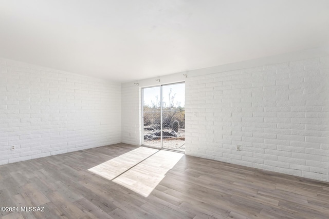 unfurnished room featuring brick wall and hardwood / wood-style flooring