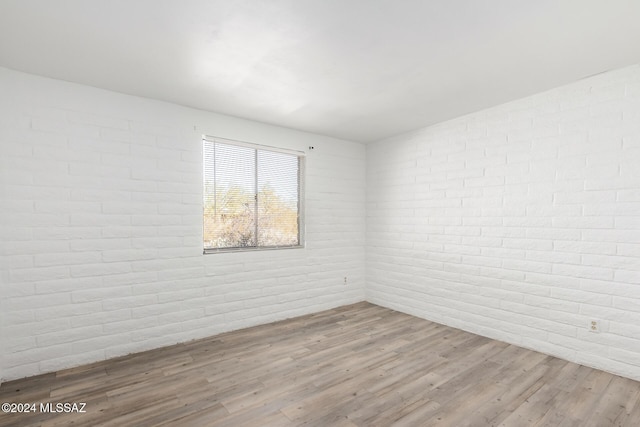 unfurnished room featuring light wood-type flooring and brick wall