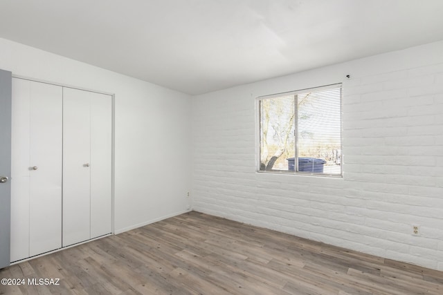 unfurnished bedroom with a closet, brick wall, and light hardwood / wood-style flooring