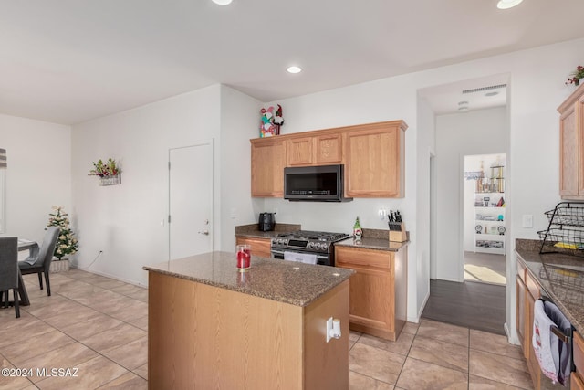 kitchen with sink, stainless steel appliances, a kitchen island, dark stone countertops, and light tile patterned flooring