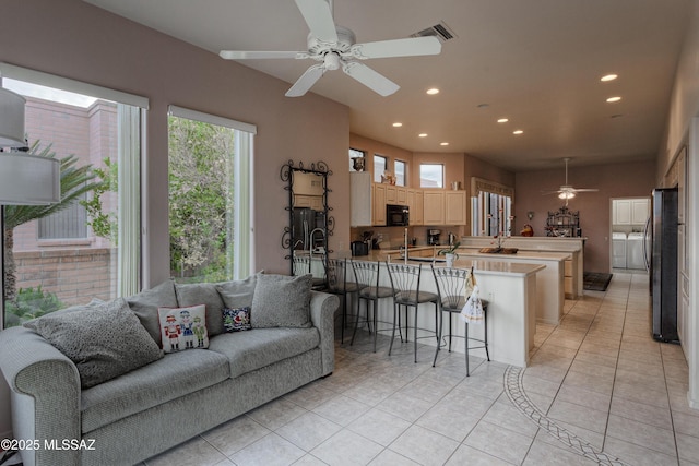 tiled living room featuring washer and dryer, ceiling fan, and sink