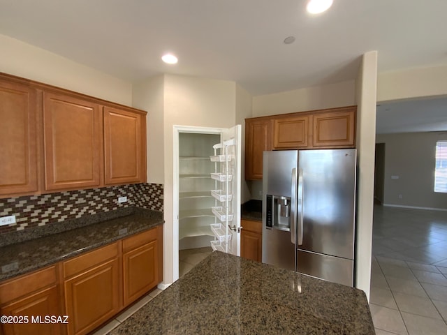 kitchen with light tile patterned flooring, dark stone counters, stainless steel fridge, and backsplash