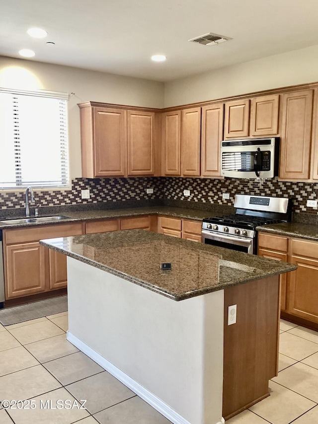 kitchen with light tile patterned flooring, a kitchen island, sink, dark stone counters, and stainless steel appliances