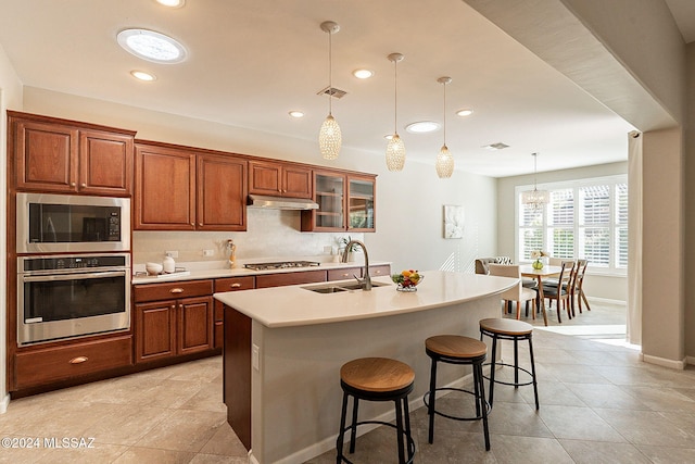 kitchen featuring a kitchen breakfast bar, stainless steel appliances, a kitchen island with sink, sink, and hanging light fixtures