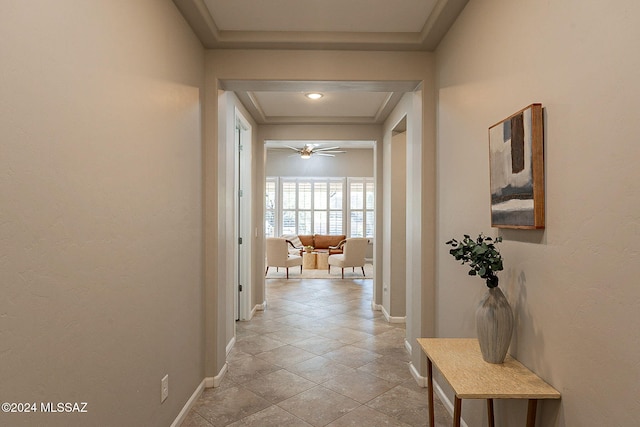 corridor with light tile patterned flooring and a tray ceiling