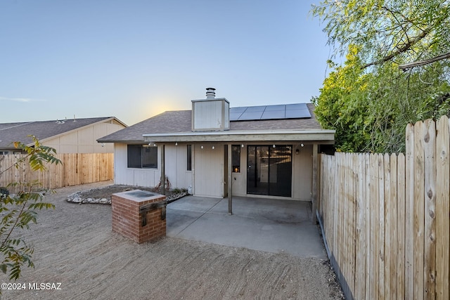 back house at dusk featuring solar panels and a patio