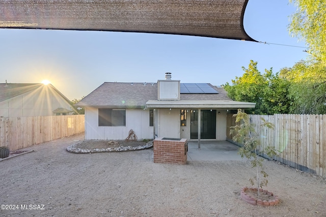 back house at dusk featuring solar panels and a patio area