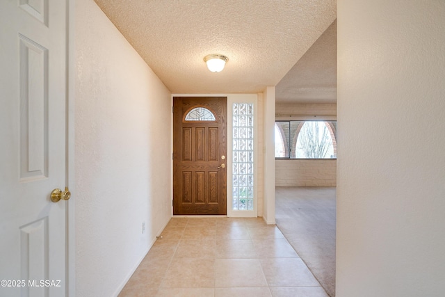 entrance foyer with light tile patterned floors, brick wall, a textured ceiling, and a textured wall