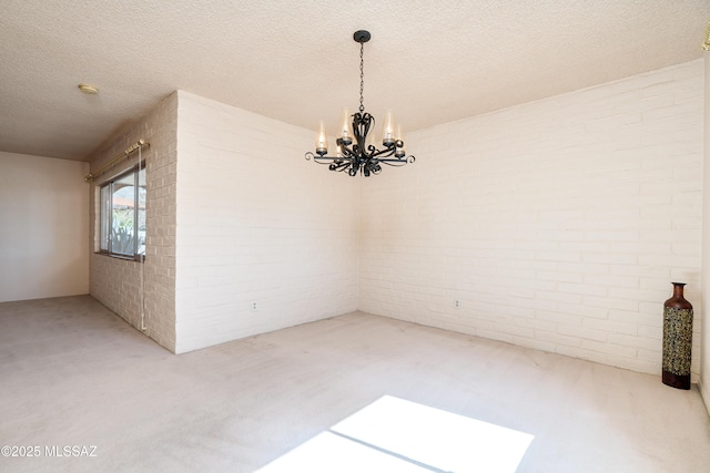 empty room featuring a textured ceiling, brick wall, and a notable chandelier